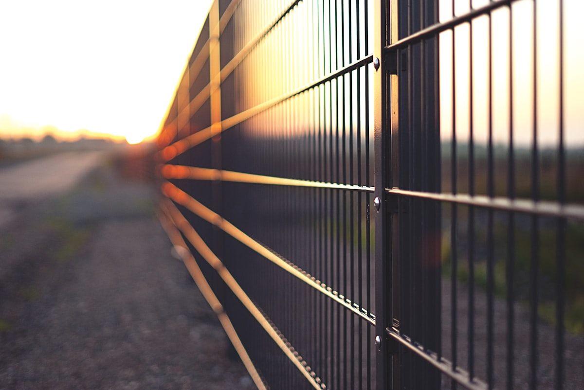 Metal security fence silhouetted against golden sunset light